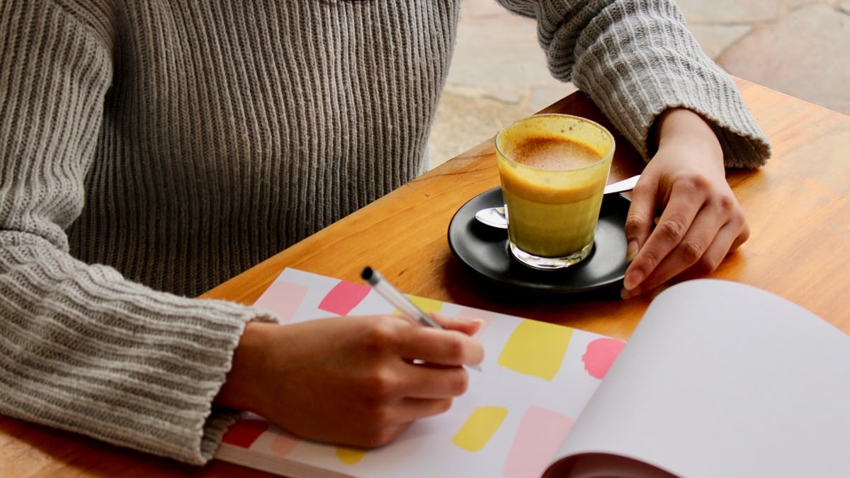 A pen resting on a weekly planner notebook next to a cup of coffee