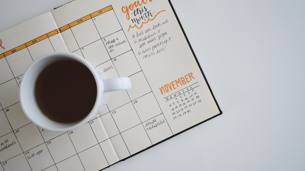 An open planner notebook with a daily schedule on a desk next to a coffee cup