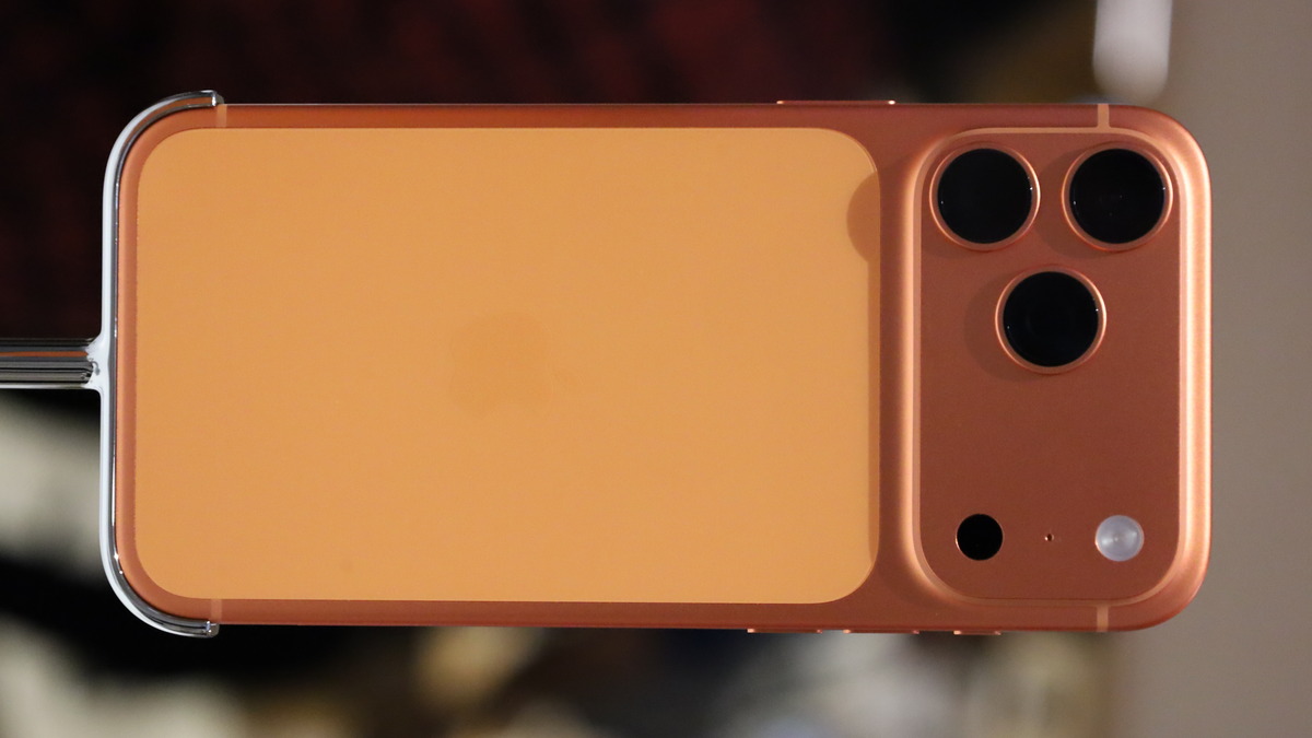 An orange-toned iPhone 17 Pro Max shown from the back, camera module visible
