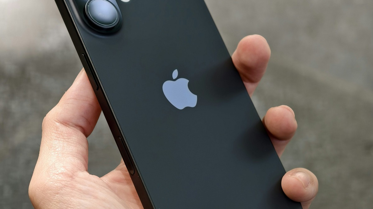 A close-up photo of a hand holding a black iPhone, showing its camera module and rear Apple logo