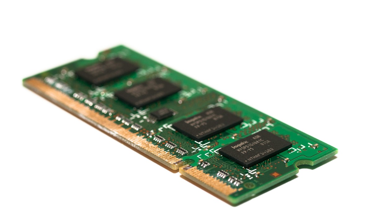 A macro product photo of a green laptop RAM module with visible memory chips and gold connector pins