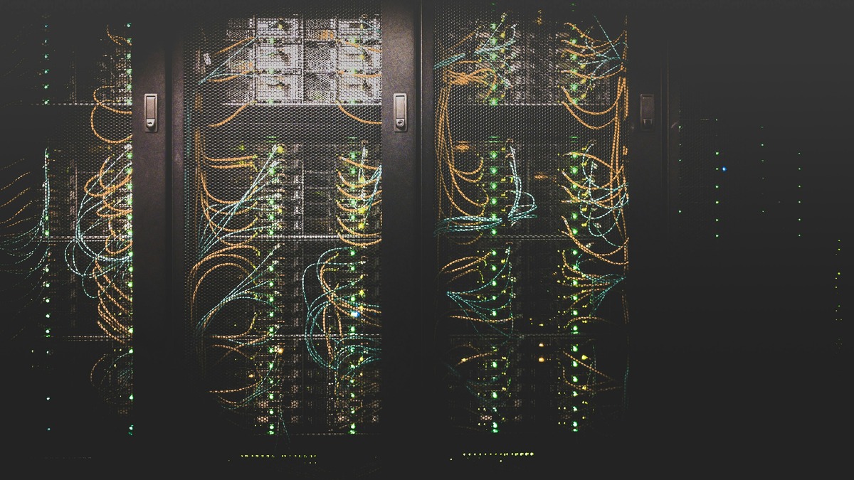 Server racks with fiber optic cables glowing orange and cyan in a dark data center