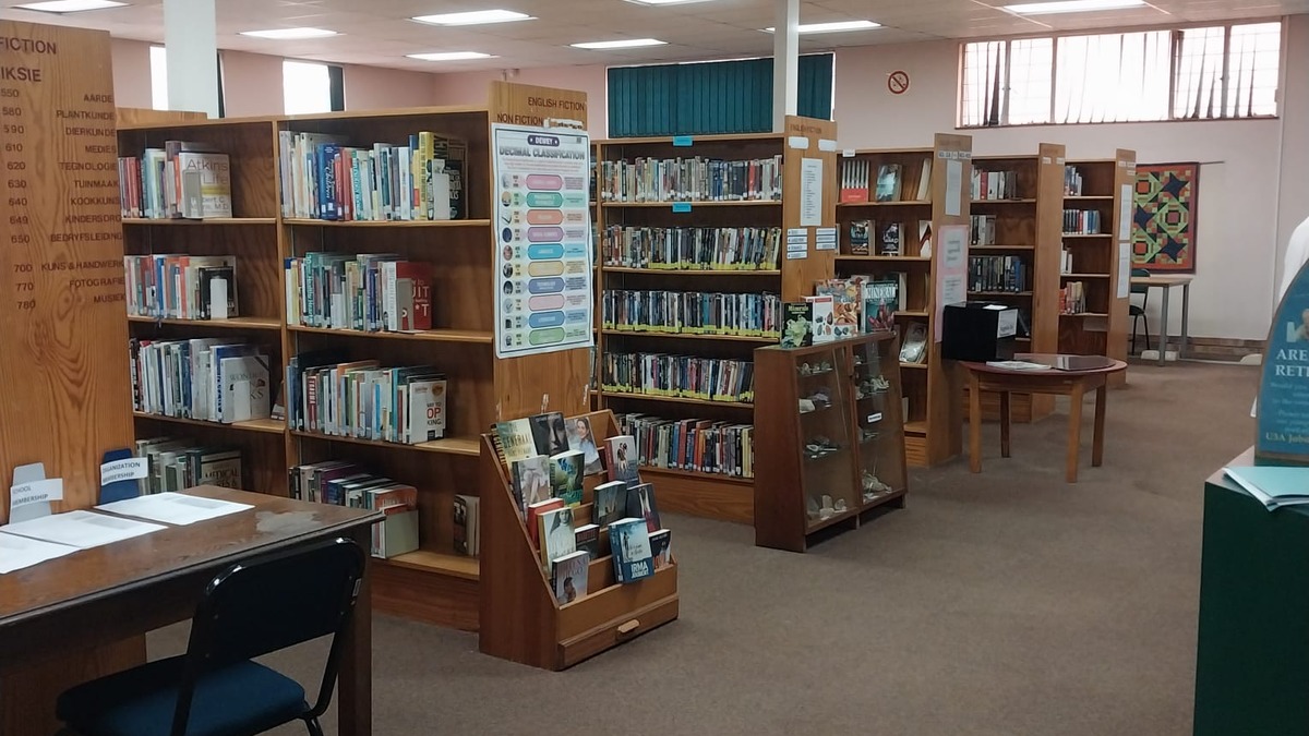A library room with wooden bookshelves lined with fiction and non-fiction titles