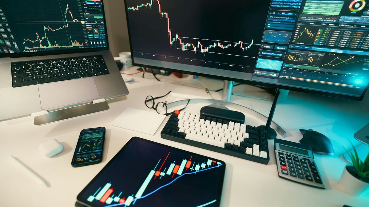 Multiple trading monitors showing candlestick stock charts on a desk