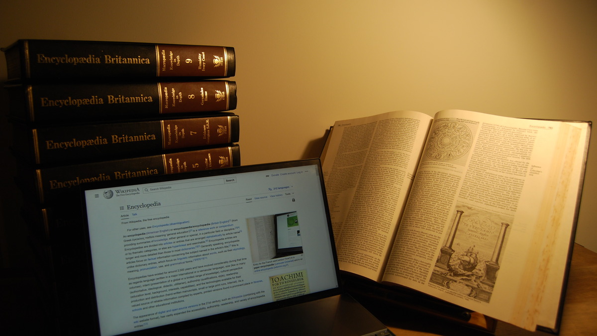 Physical copy of Encyclopaedia Britannica next to a laptop showing Wikipedia's encyclopedia article