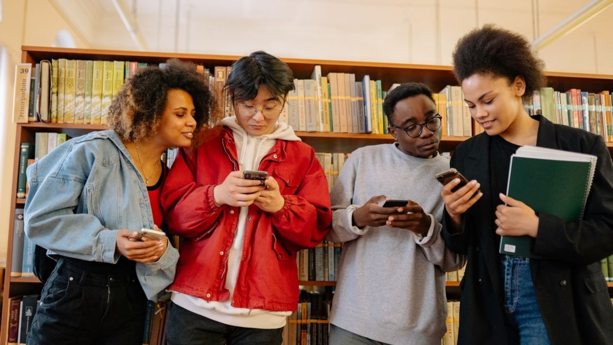 A diverse group of students using smartphones together in a library setting