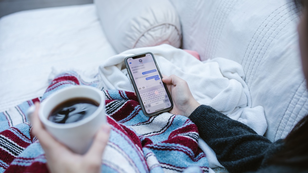 Person relaxing with smartphone and coffee, looking at screen in a cozy setting