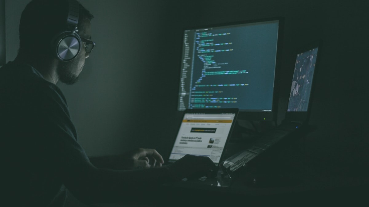 Security researcher at multiple monitors reviewing code output in a dark room