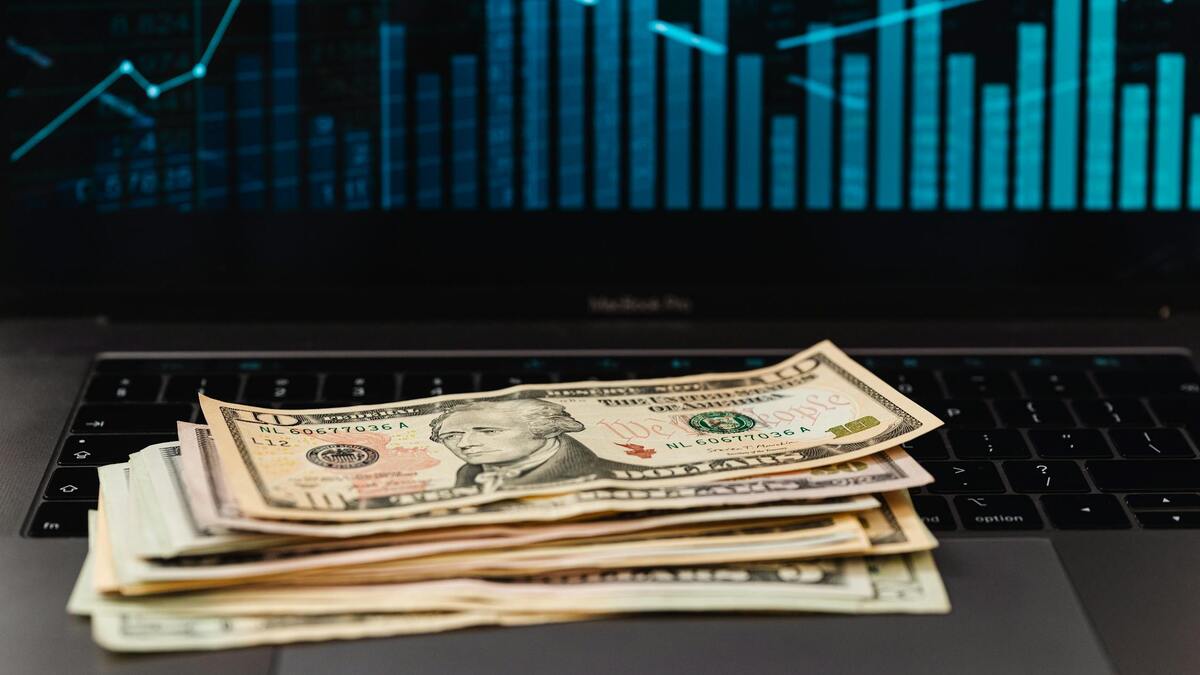 Dollar bills on a laptop keyboard with financial charts