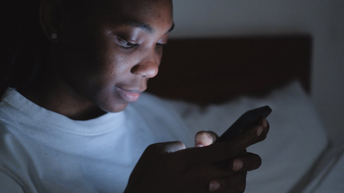 A person lying in a dark room, face lit only by a phone screen