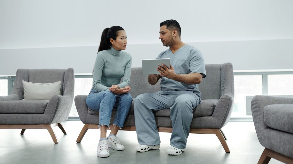 A doctor consults with a patient while holding a tablet in a clinic waiting area