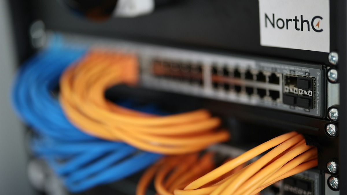 A network switch in a data center rack with blue and orange ethernet cables plugged into multiple ports