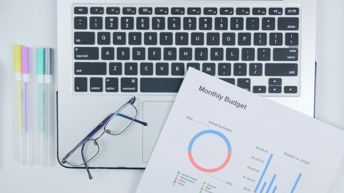 A printed budget report spreadsheet on a modern desk with a laptop
