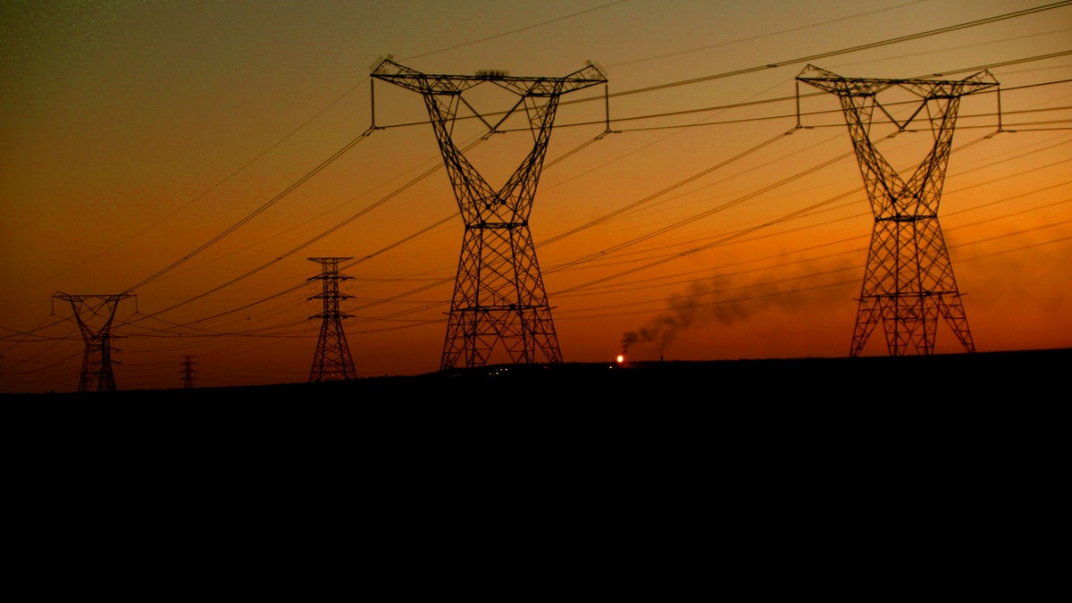 Electrical transmission towers silhouetted against an orange sunset sky