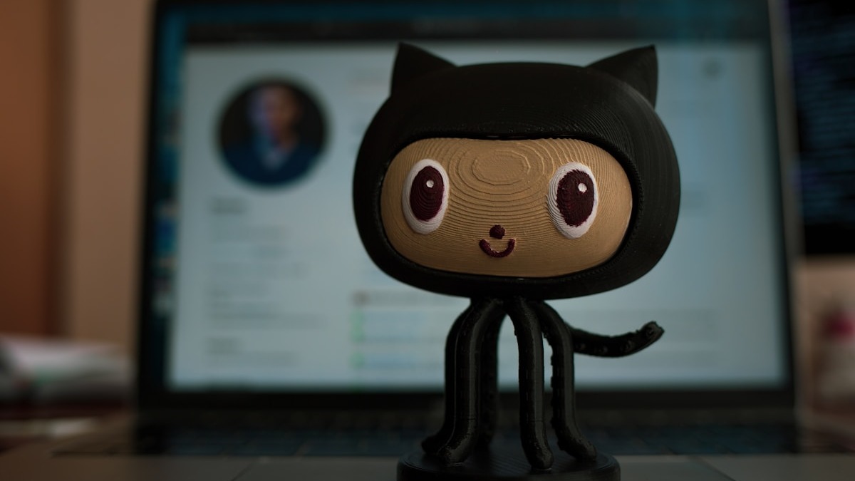 GitHub Octocat figurine in front of a laptop with a GitHub profile page