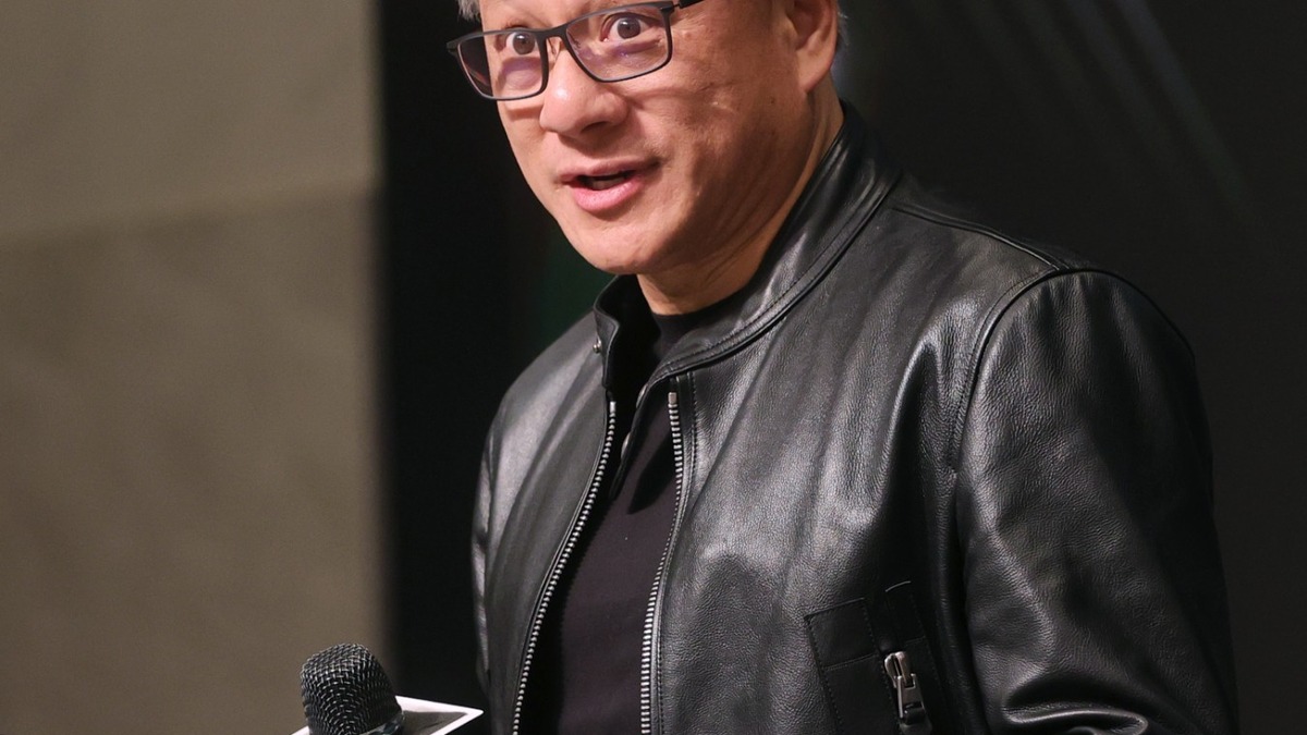 Jensen Huang speaking at a press event, wearing his signature leather jacket