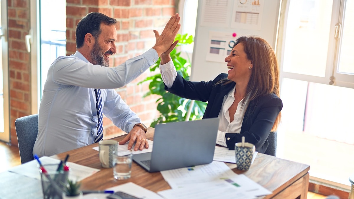 Two business professionals celebrate a deal at an office desk