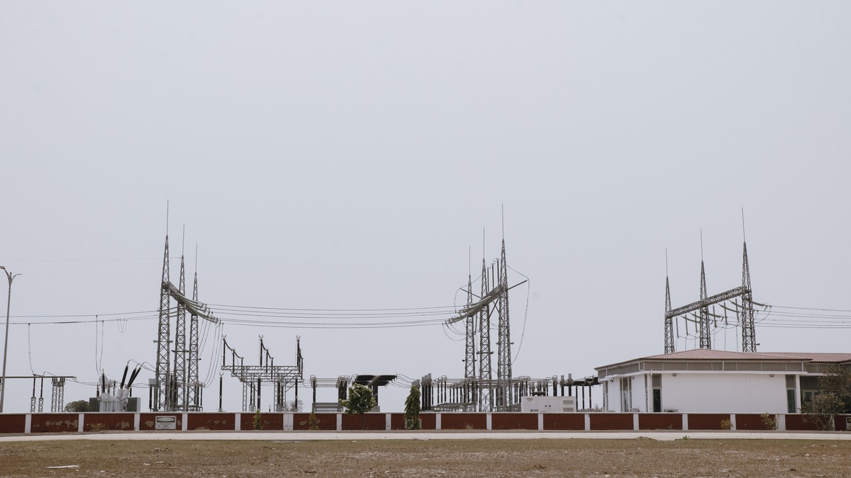 A substation with high-voltage transmission towers and transformer equipment behind a low wall