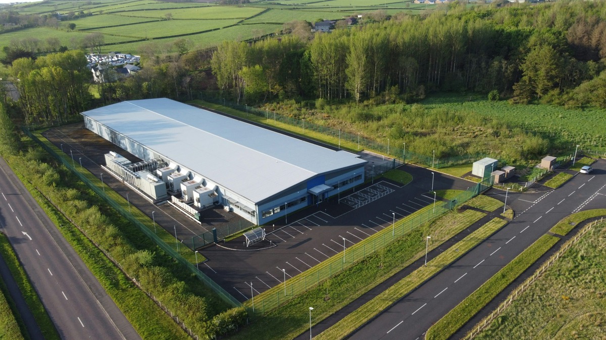 Aerial view of a data center building with rooftop cooling equipment surrounded by green fields