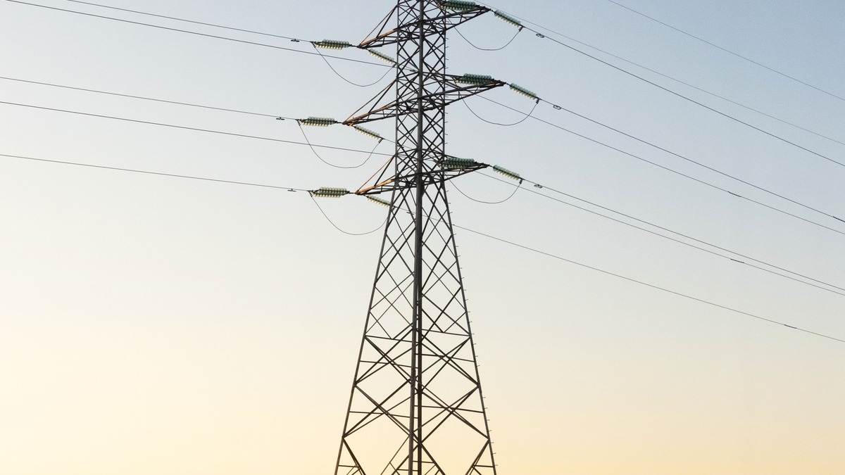 A high-voltage electricity transmission tower silhouetted against a sunset sky