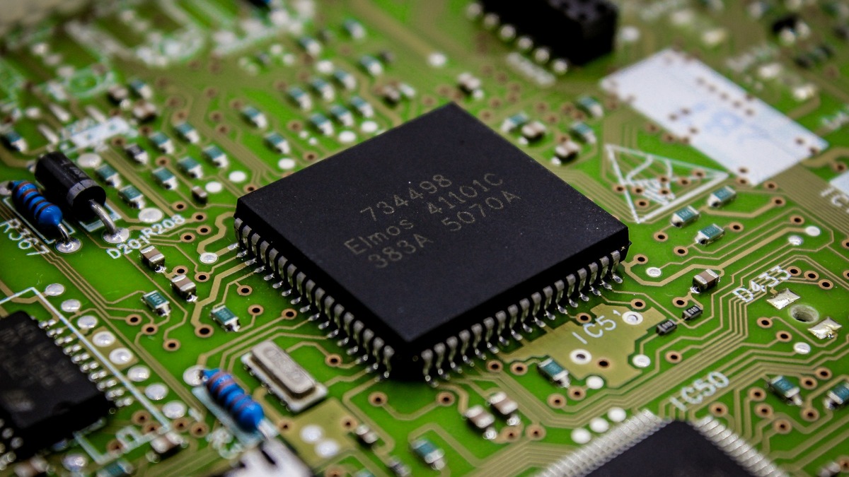 A green circuit board with a black chip package soldered at its center, surrounded by resistors and capacitors