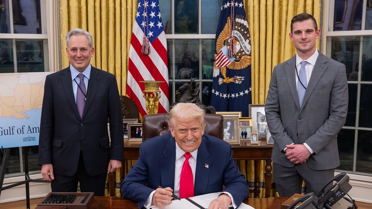 Donald Trump signs an executive order in the Oval Office, flanked by two administration officials