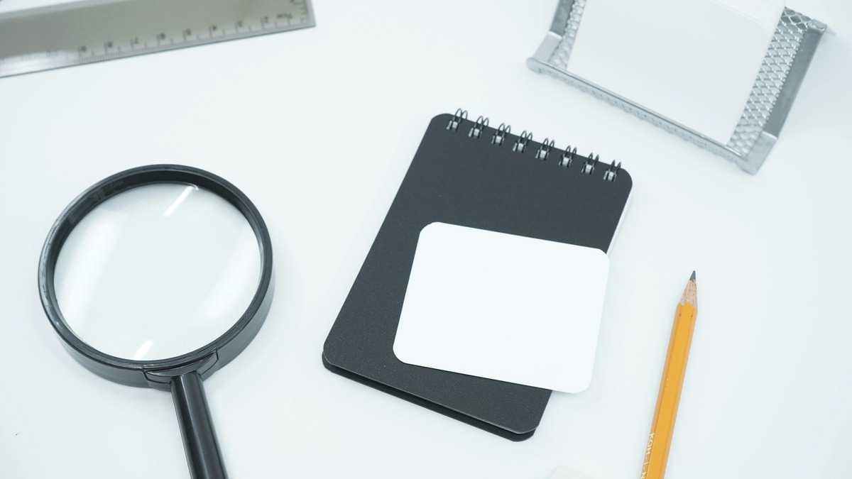 Black magnifying glass resting on white paper with a notepad and pencil nearby
