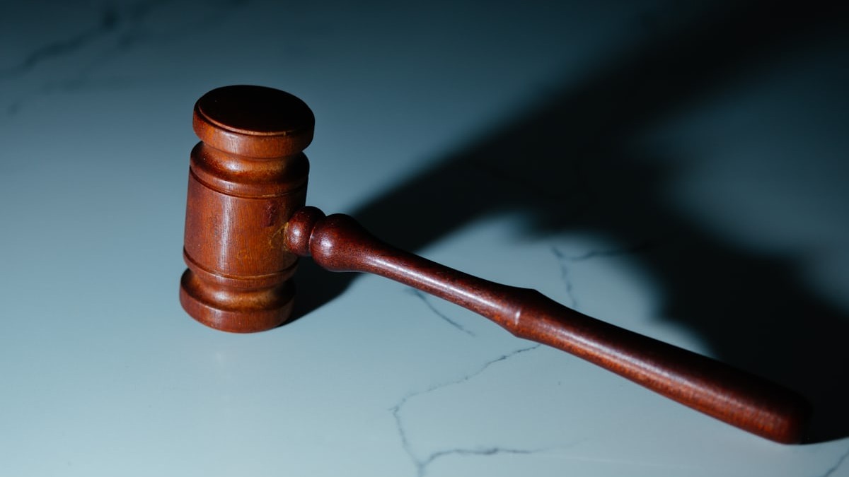 A wooden gavel rests on a marble surface, its shadow stretching diagonally across the stone