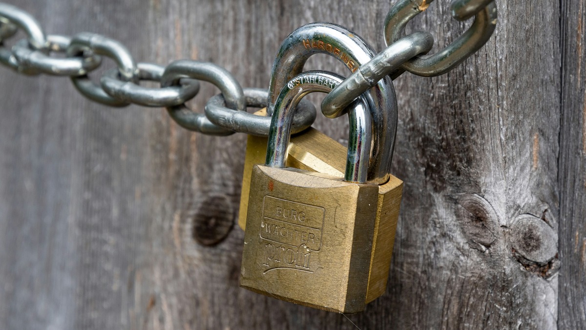 A brown padlock securing a wooden fence in an outdoor setting