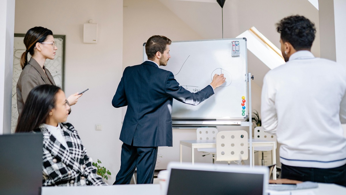 A team collaborating at a whiteboard, the real-world equivalent of what Miro aims to digitize