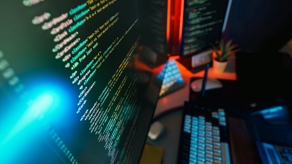 Multiple computer screens showing code in a dark developer workspace