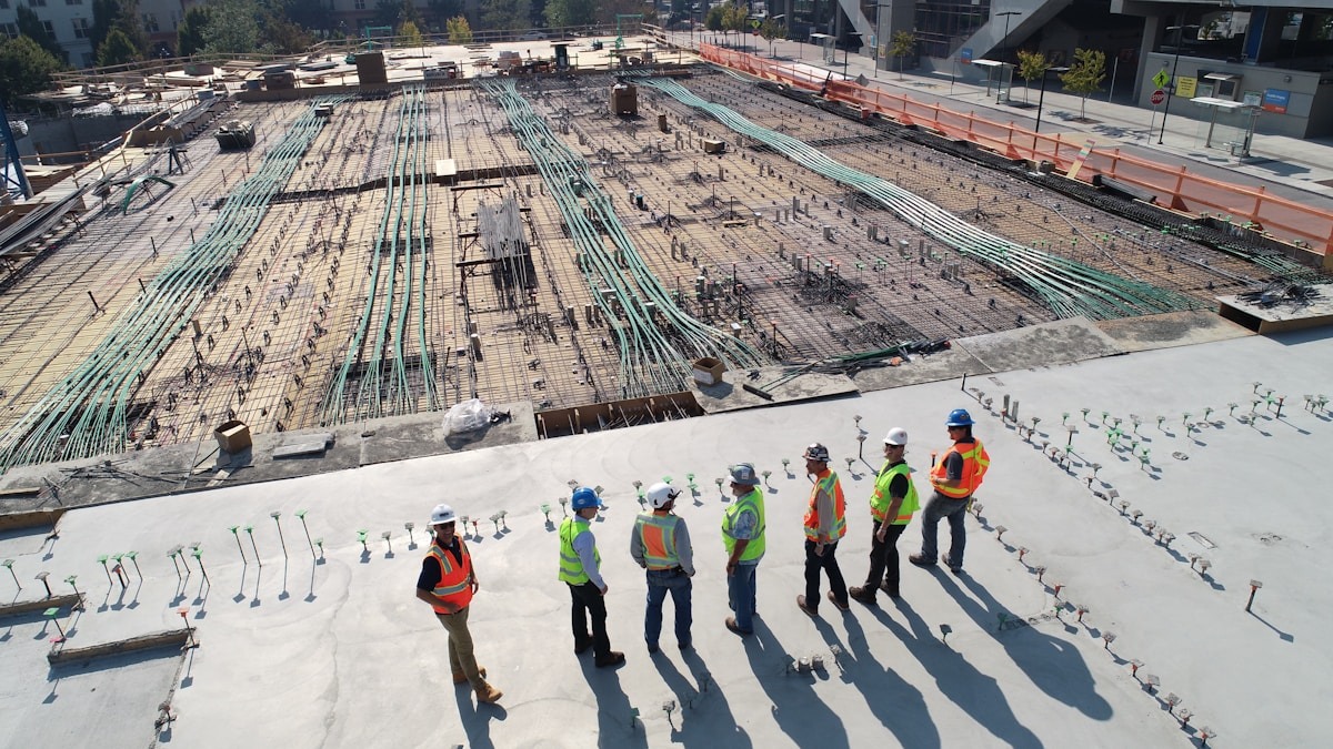 A project manager reviewing digital construction plans on a tablet at a job site with a building under construction visible in the background