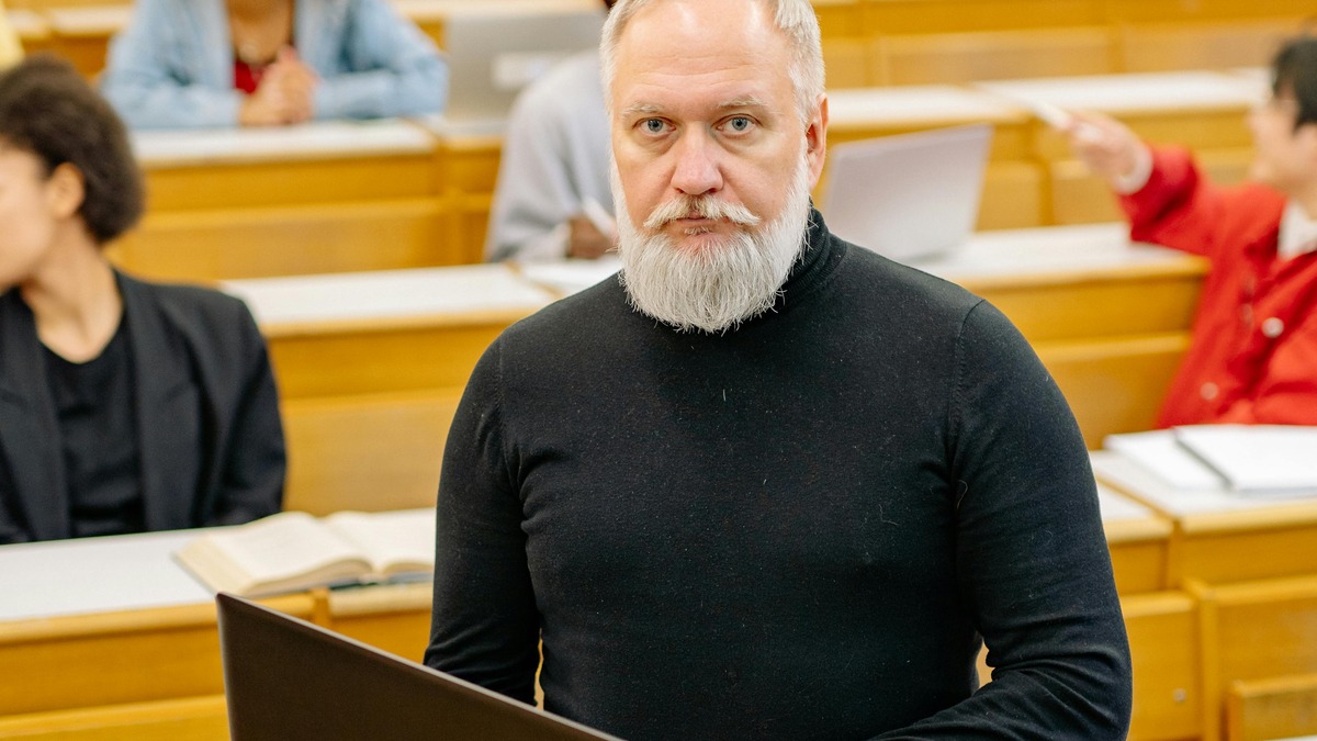 A university professor reviewing student progress on a laptop in a classroom