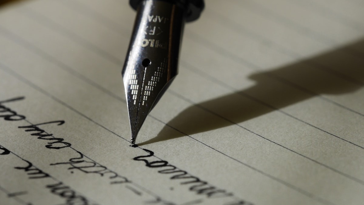 Open notebook with pen on a wooden desk next to a coffee cup