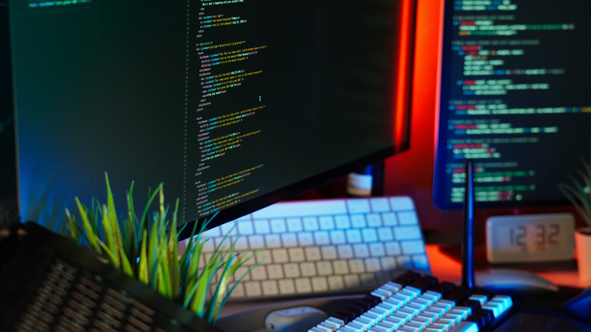 Code flowing across multiple monitors in an orange and dark-blue developer workspace