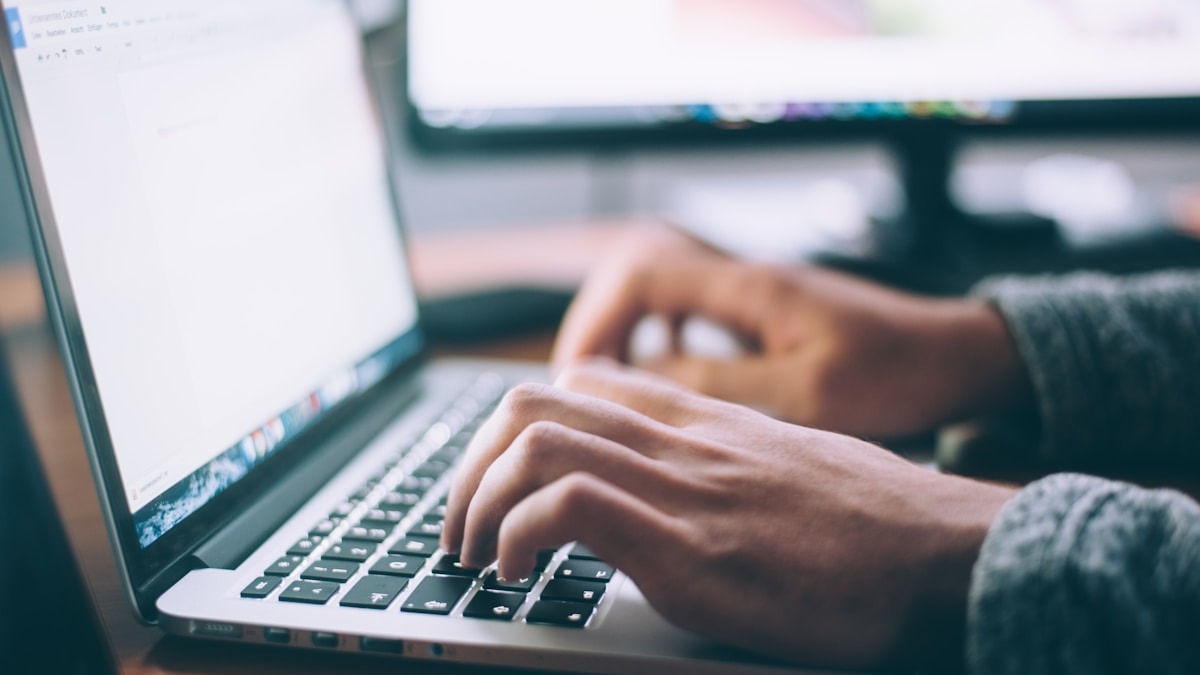 Person typing on laptop at a clean bright desk with notebook and coffee cup alongside
