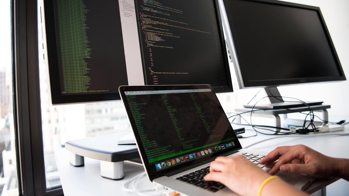 Developer in a dimly lit workspace, hands on keyboard with code visible on screen